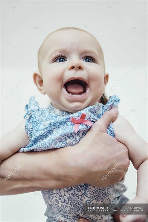 Portrait Of Screaming Baby Girl Holding By Human Hands — Front View