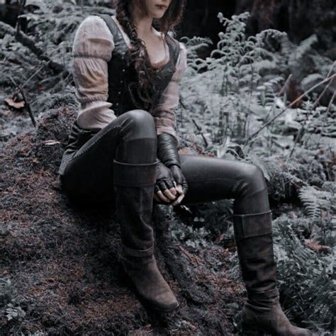 a woman sitting on top of a tree stump in the middle of a forest wearing boots