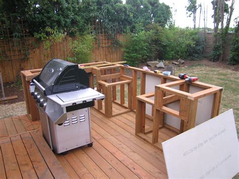 An Outdoor Bbq Grill On A Wooden Deck In The Middle Of A Backyard Area