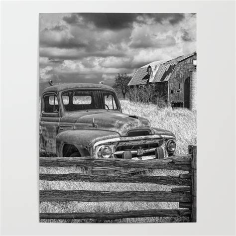black and white of rusted international harvester pickup truck behind wooden fence with red barn