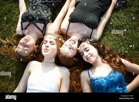 Four Teenage Girls Wearing Daisy Chain Headdresses Lying On Park Grass