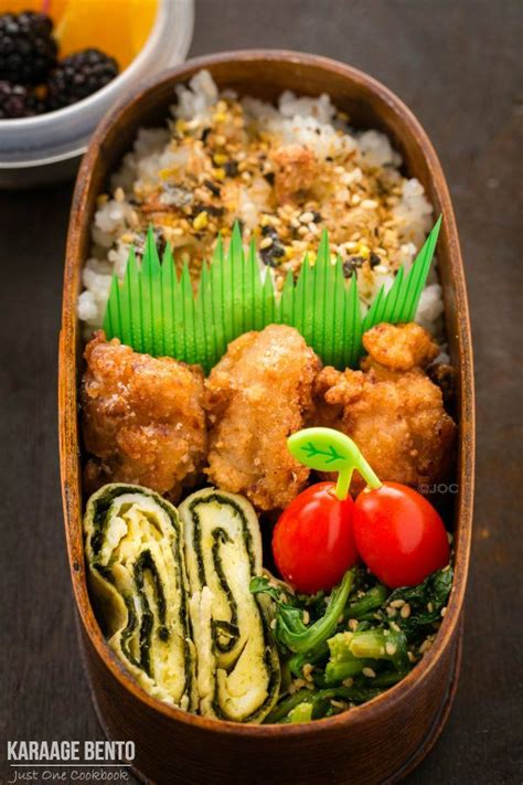 A Bento Box Filled With Rice Meat And Veggies Next To A Bowl Of Fruit