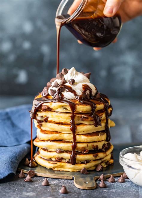 A Stack Of Pancakes Topped With Whipped Cream And Chocolate Syrup Being