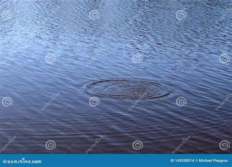 Blue Lake Water Surface With Ripples And Splashing Item Falling Into It