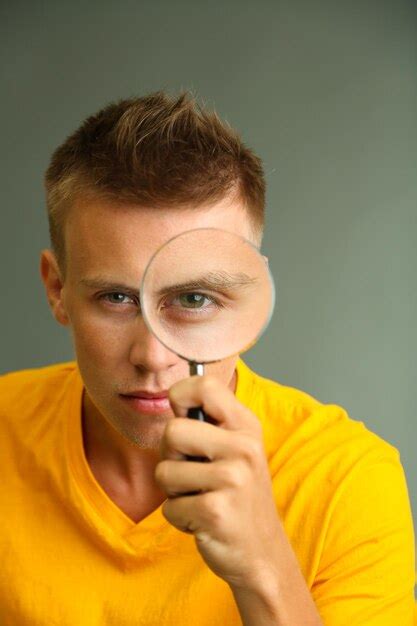 Premium Photo Young Man Looking Through Magnifying Glass On Grey