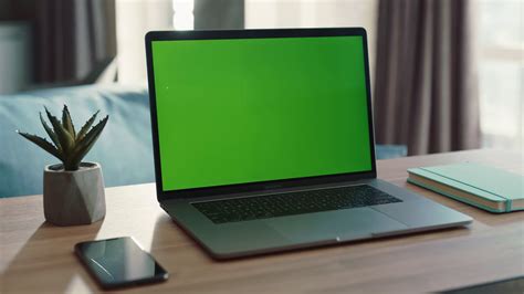 Laptop with green screen on desk with smartphone and notebook near the ...