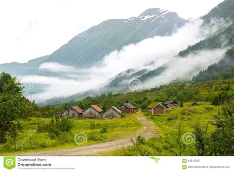 Landscape With Old Wooden Houses And Mountains Covered By Clouds