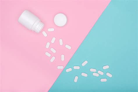 medication bottle and white pills spilled on blue and pink pastel coloured background medication