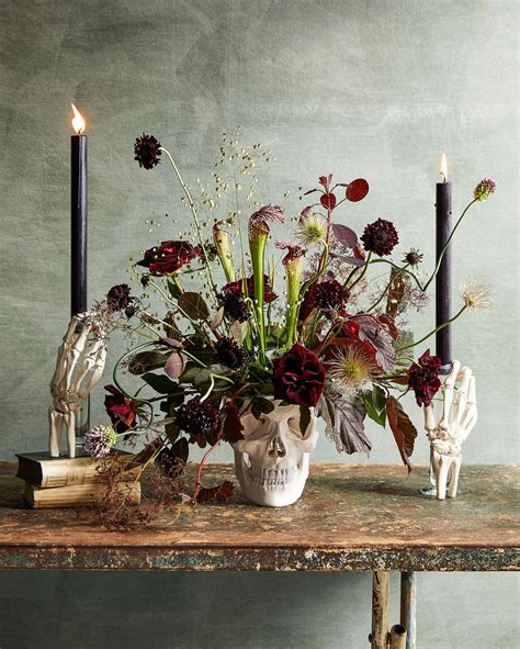A Table Topped With A Skull Vase Filled With Flowers And Two Candles