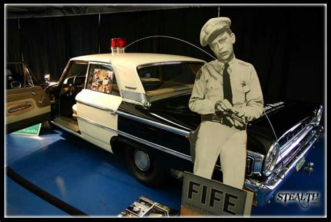 An Old Fashioned Car On Display With A Man In Uniform Standing Next To