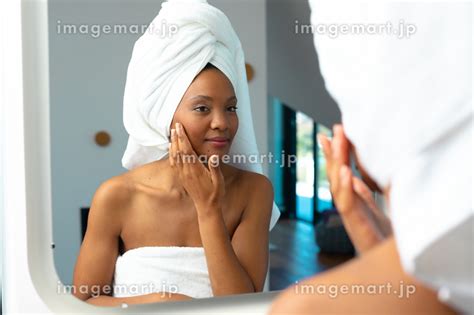 African American Young Woman Touching Her Cheek While Looking In Mirror At Home Unaltered Spa