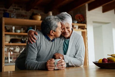 Happily Elderly Biracial Couple Enjoying Retirement Wife Holding Husband In Modern Kitchen