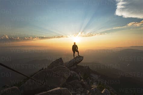Man Standing On Rock At Cliff Against Sky During Sunset Stock Photo