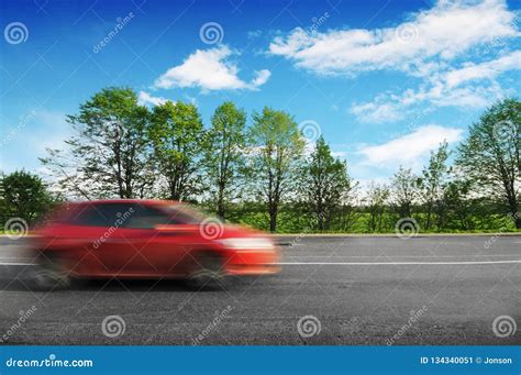 A Red Car Driving Fast On The Countryside Road With Trees And Bushes