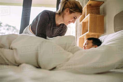 Young Mother And Her Son Playing Together On The Bed At Home Woman Having Fun With Her Son At