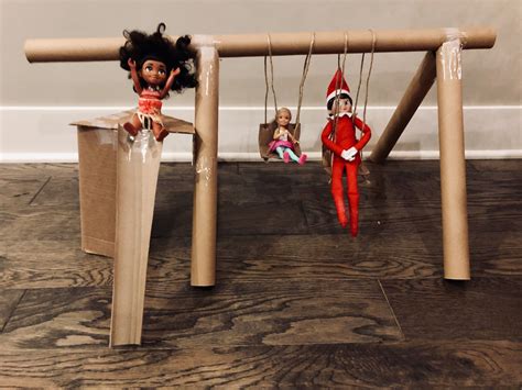 two elf dolls are sitting on the swings in front of a cardboard box with strings attached to it
