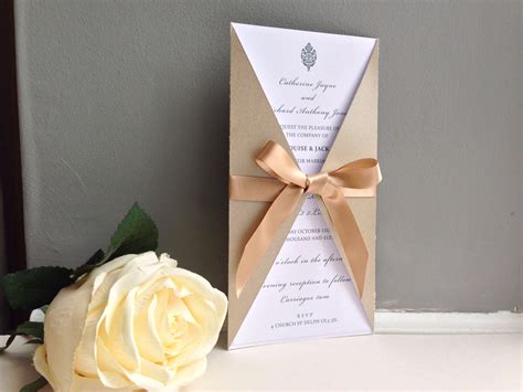 A White Rose Sitting Next To A Brown And Beige Wedding Stationery On A