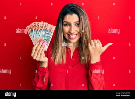 Beautiful Brunette Woman Holding Australian 20 Dollars Pointing Thumb Up To The Side Smiling