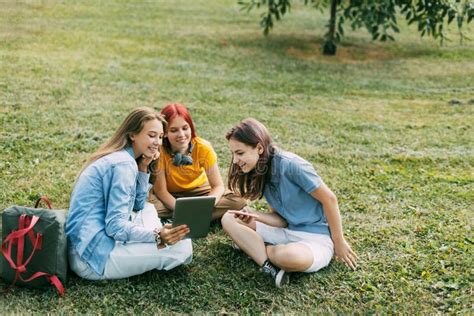 Teenage Girls Sit On The Green Lawn In The Park During A Break