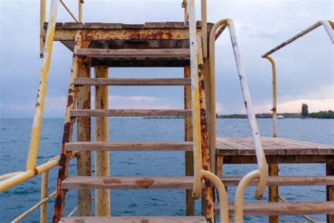 Large Pier With A Roof And A Rusty Staircase Descending Into The Water