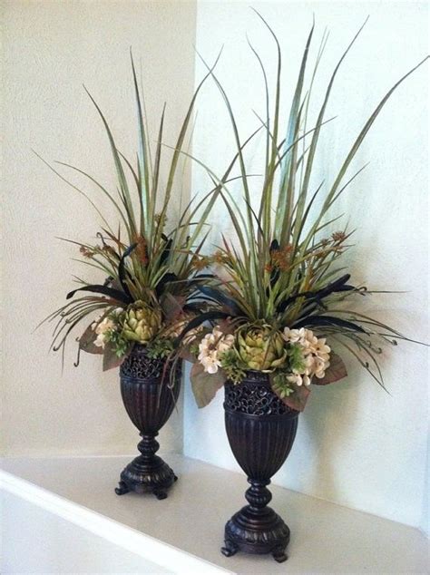 Two Black Vases Filled With Plants On Top Of A White Shelf Next To Each