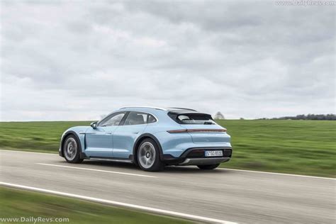 A Blue Porsche Suv Driving Down The Road In Front Of A Green Grass