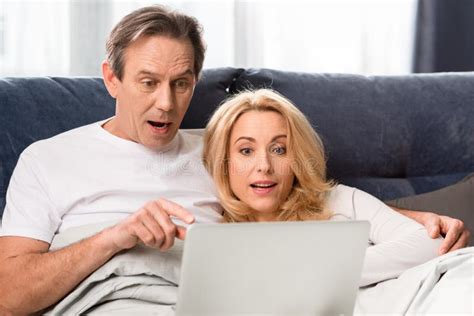 Middle Aged Couple Using Laptop And Lying On Bed At Home Stock Image