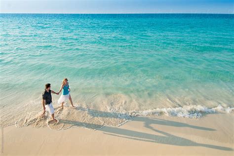 Aerial View Of Romantic Couple Walking Along Tropical Caribbean Beach During Luxury Vacation