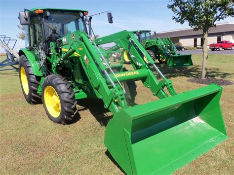 A Green Tractor Parked In The Grass Next To A Plow And Two Other Tractors