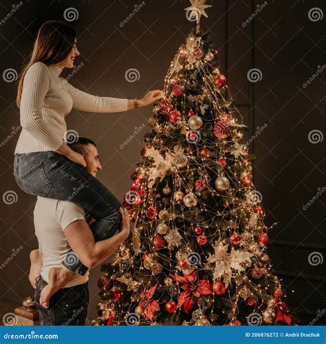 Jonge Vrouw Zit Op De Achterste Schouders Van De Man En Versiert Een Kerstboom Stock Foto