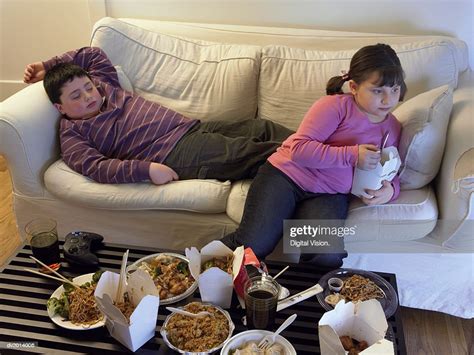 Overweight Brother And Sister On A Sofa Eating Takeaway Food And Watching The Tv High Res Stock