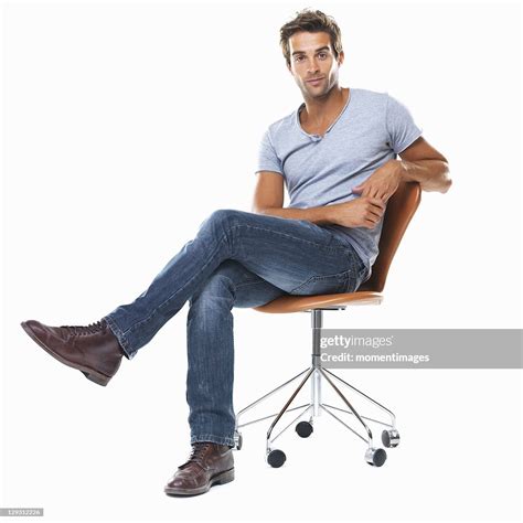 Portrait Of Young Man Sitting On Chair With Legs Crossed Against White