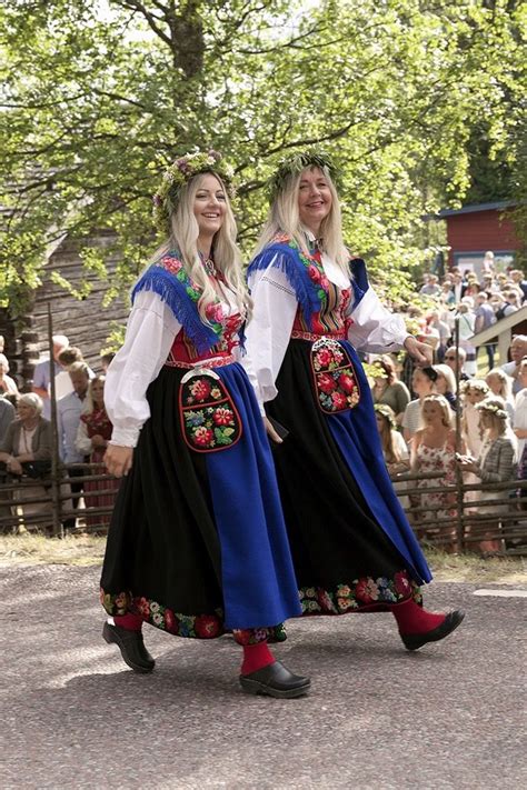 two women dressed in folk clothing walking down the street while people watch from behind them