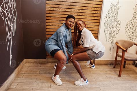 Two African Womans In Stylish Casual Clothes Posing Against Wooden Wall