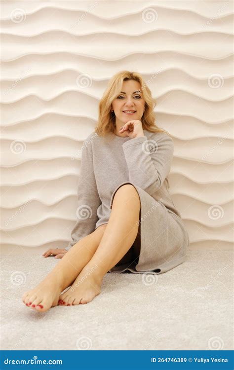 A Beautiful Slim Mature Woman Is Sitting On A Carpet In A Dress With A