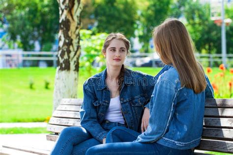 two beautiful girlfriends are talking in a park sitting on a bench stock image image of