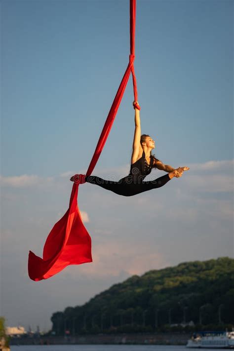 beautiful and flexible female circus artist dancing with aerial silk on a sky background stock