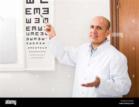 Elderly Male Ophthalmologist Pointing At Letters Of Eye Chart Stock