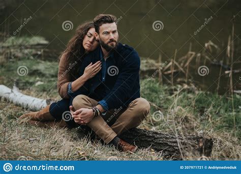 Two Caucasian Lovers Are Sitting On The Shore Of The Lake Young Couple Is Hugging On Autumn Day