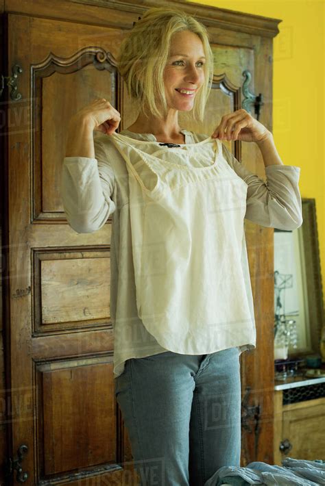 Mature Woman Standing In Bedroom Holding Blouse Against Her Chest And