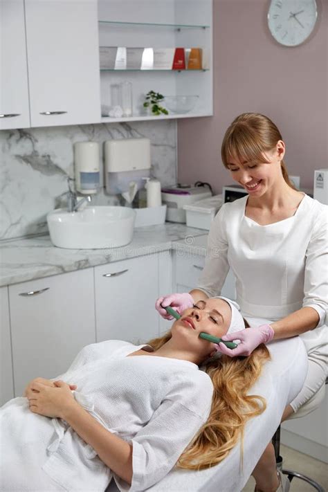 Young Woman Receiving Facial Massage With Stone Sticks In Beauty Salon