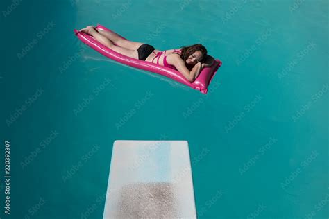 Diving Board And Young Woman In A Bikini On A Raft On Her Stomach In An Outdoor Swimming Pool