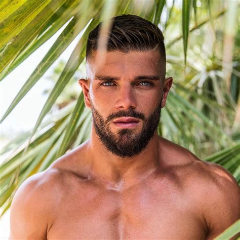A Man With No Shirt On Standing In Front Of Palm Trees And Looking At The Camera