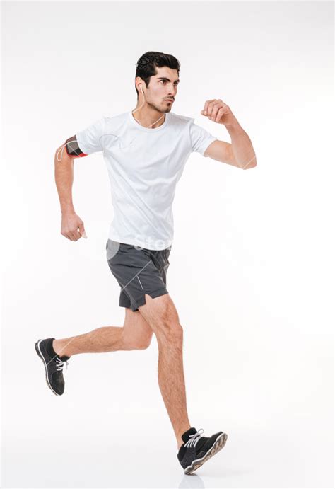 Side View Of A Focused Young Athlete Running With Earphones On A White