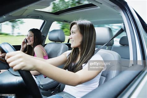 Two Teenage Girls Driving In Car One Girl With Mobile Phone High Res