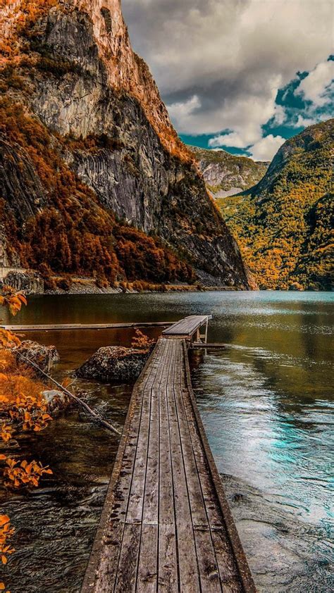 A Wooden Dock Sitting On Top Of A Lake Surrounded By Mountains