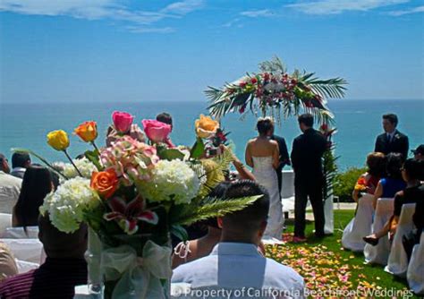 Bride is standing on the beach in front of wedding arch, decorated in boho style with orchid flowers sea at summer sunny day. Southern California Beachfront Weddings / Orange County ...