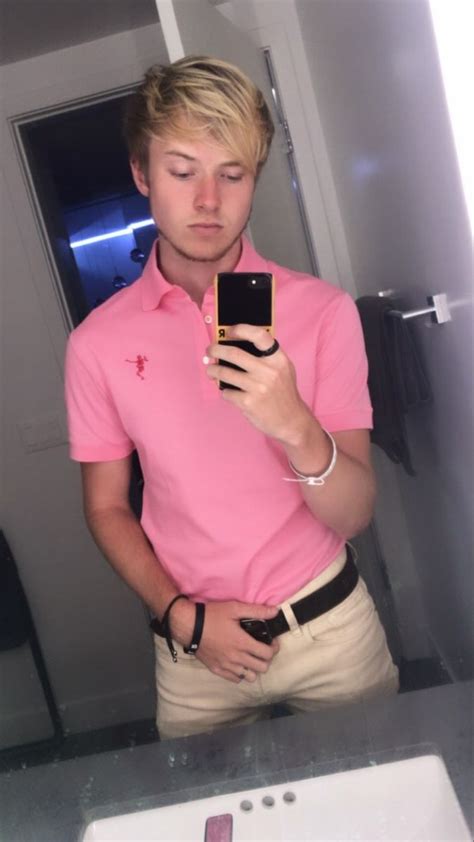 A Man In A Pink Shirt Is Looking At His Cell Phone And Taking A Selfie