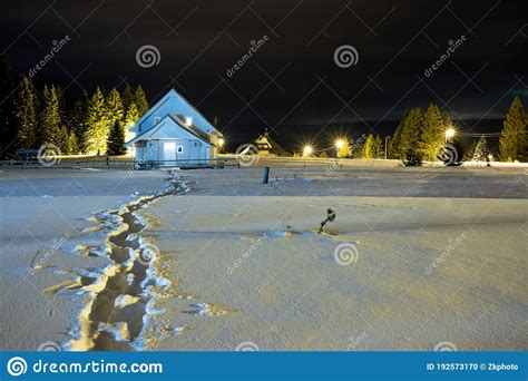 Traces In The Snow Leading To Small House House Isolated At Night In