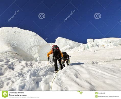 Two Mountain Climbers Headed To A High Alpine Peak Over A Steep Glacier